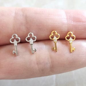 Puede incluir: Cuatro pendientes con forma de llave. Dos son plateados y dos dorados. Cada llave tiene una parte superior en forma de tr&eacute;bol y una peque&ntilde;a gema transparente. Los pendientes son peque&ntilde;os y delicados.
