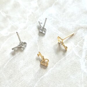 Puede incluir: Cuatro pendientes con forma de llave en tonos plateados y dorados est&aacute;n dispersos sobre una superficie clara. Los pendientes presentan dise&ntilde;os de ojo de cerradura y lazo, mostrando una delicada est&eacute;tica de joyer&iacute;a.