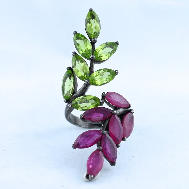 Pu&ograve; includere: Anello color argento con design a foglia, incastonato con pietre preziose taglio marquise. La parte superiore della foglia &egrave; adornata con pietre di peridoto verde brillante, mentre la sezione inferiore presenta rubini rosso scuro.