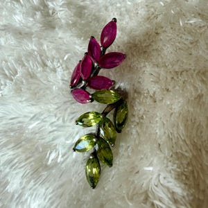 Pu&ograve; includere: Spilla argentata a forma di foglia, con due sezioni di pietre preziose taglio marquise. La sezione superiore presenta pietre rosa intenso, mentre la sezione inferiore ha pietre verde chiaro. Su sfondo bianco e soffice.