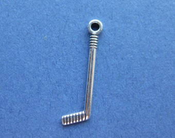 Könnte beinhalten: Ein silberner Hockey-Schläger-Anhänger mit einer Öse zum Befestigen an einem Armband oder einer Halskette. Der Schläger hat ein detailliertes Design mit geripptem Griff und gebogener Klinge.