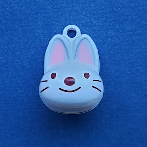 May include: White ceramic bunny charm with pink ears and brown eyes. The bunny has a smiling mouth and a small bell on the back.