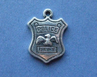 May include: A silver-colored Police Dept. badge charm. The shield-shaped charm features the word "POLICE" at the top, an eagle in the center, and the word "DEPT" at the bottom. The charm has a loop at the top for attaching to a necklace or bracelet.