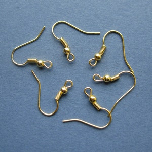 May include: Five gold-colored earring hooks are arranged on a blue background. Each hook features a curved wire, a coiled spring, a small bead, and a loop for attaching earrings. The hooks are made of a shiny, metallic material.