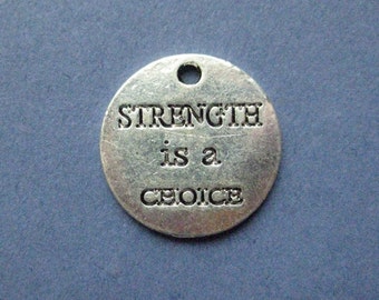 May include: A round, silver-toned metal charm with the words "STRENGTH is a CHOICE" engraved in capital letters. The charm has a small hole at the top for attaching to a chain or other item. The background is a solid, muted blue.