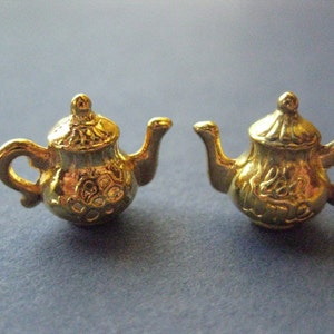 May include: A pair of gold-tone teapot earrings with intricate details. The teapots have a rounded body with a spout and handle.