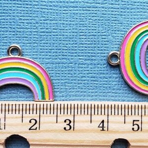 K&ouml;nnte beinhalten: Zwei regenbogenfarbene Metall-Anh&auml;nger mit silberner Oberfl&auml;che. Die Anh&auml;nger sind regenbogenf&ouml;rmig mit einer &Ouml;se oben zum Anbringen an einer Halskette oder einem Armband. Die Anh&auml;nger sind etwa 2,5 cm gro&szlig;.