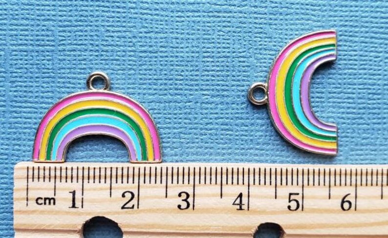 K&ouml;nnte beinhalten: Zwei regenbogenfarbene Metall-Anh&auml;nger mit silberner Oberfl&auml;che. Die Anh&auml;nger sind regenbogenf&ouml;rmig mit einer &Ouml;se oben zum Anbringen an einer Halskette oder einem Armband. Die Anh&auml;nger sind etwa 2,5 cm gro&szlig;.