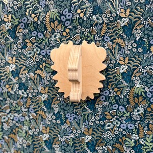 May include: A wooden wall-mounted decorative piece shaped like a lion's head with a textured surface. The piece is painted in a light brown color and is set against a dark blue background with a floral pattern.