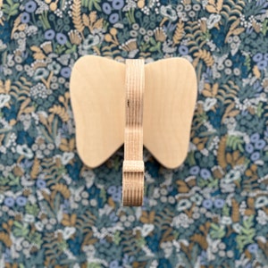 Puede incluir: Una decoraci&oacute;n de pared de madera en forma de mariposa con un acabado de madera natural. La mariposa est&aacute; hecha de madera contrachapada y tiene un dise&ntilde;o simple y elegante.