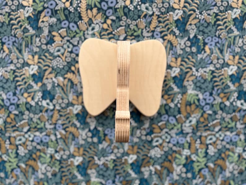 Puede incluir: Una decoraci&oacute;n de pared de madera en forma de mariposa con un acabado de madera natural. La mariposa est&aacute; hecha de madera contrachapada y tiene un dise&ntilde;o simple y elegante.