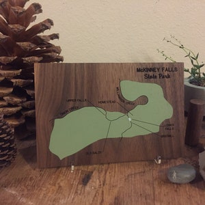 May include: A wooden map of McKinney Falls State Park in Texas. The map shows the park's trails, creeks, and other features. The map is mounted on a wooden stand.