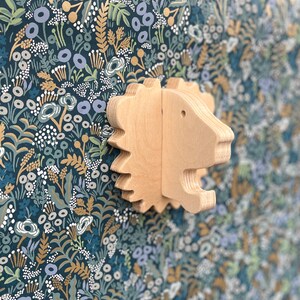May include: A wooden lion head wall decor with a light brown finish. The lion head is carved with intricate details and has a whimsical, playful look. It is a great addition to a child's room or nursery.