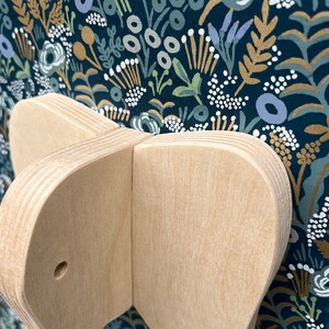 Puede incluir: Primer plano de un juguete de madera con forma de mariposa con un agujero en el centro. El juguete est&aacute; hecho de madera clara y tiene un acabado liso y pulido.