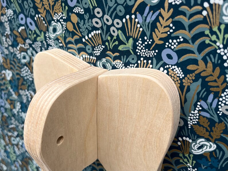 Puede incluir: Primer plano de un juguete de madera con forma de mariposa con un agujero en el centro. El juguete est&aacute; hecho de madera clara y tiene un acabado liso y pulido.