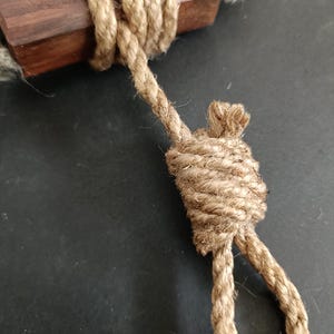 Może przedstawiać: Zbliżenie na zawiązany sznur z brązowej juty. Sznur jest owinięty wokół kawałka drewna.