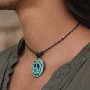 May include: A peace sign pendant necklace. The pendant is oval-shaped with a blue peace symbol in the center, surrounded by a green and white design. The necklace has a black cord.