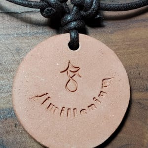 May include: A round, reddish-brown pendant necklace with a black cord. The pendant has an etched design and the word "millennium" inscribed around the bottom. The cord is knotted at the top.