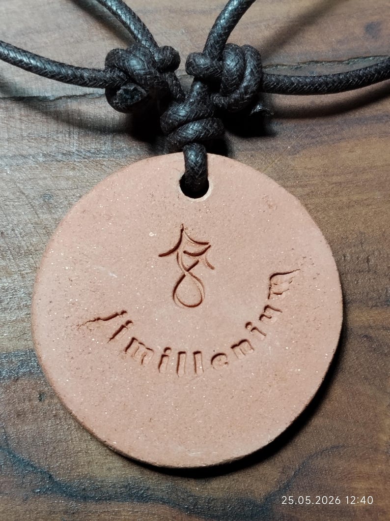 May include: A round, reddish-brown pendant necklace with a black cord. The pendant has an etched design and the word "millennium" inscribed around the bottom. The cord is knotted at the top.