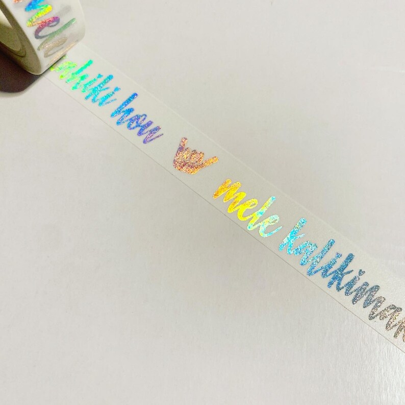 May include: A roll of iridescent holographic washi tape with the text "Aloha" and "mele kalikimaka" in rainbow colors.