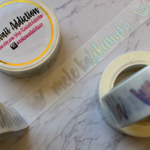 May include: Three rolls of white washi tape with holographic lettering. The tape reads "Kawaii Addiction", "@xokawaiailohaxo", and "mele kalikimaka".