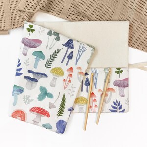 May include: A cream-coloured crochet hook case featuring a vibrant mushroom pattern. The case is open, displaying two wooden crochet hooks. The mushroom design includes red, blue, green, and yellow fungi on a white background.
