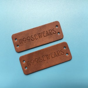 May include: Two brown leather labels with the text "MOOSEWEARS" embossed on them. Each label has four holes punched in the corners.