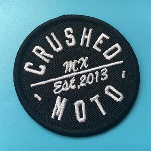May include: Black and white embroidered patch with the text "CRUSHED MOTO" in a circle. The text "MCX Est. 2013" is written in a smaller font inside the circle.