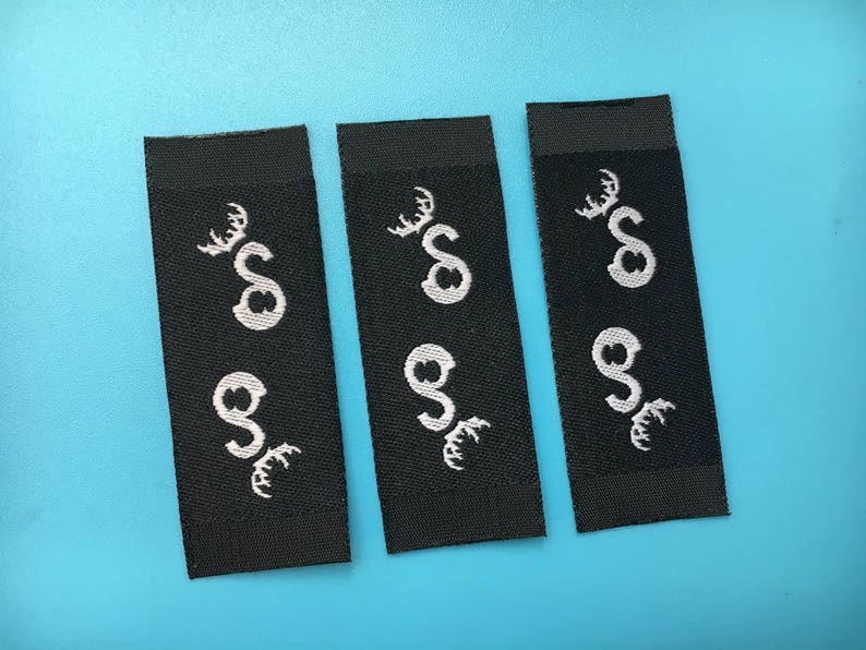 May include: Three black fabric labels with white embroidered designs. Each label features a stylized deer head with antlers and the letter "S" inside the head.