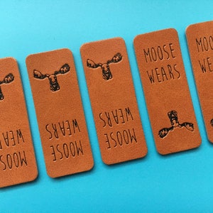 May include: Five brown leather tags with the text "Moose wears" and a moose silhouette printed on each tag.