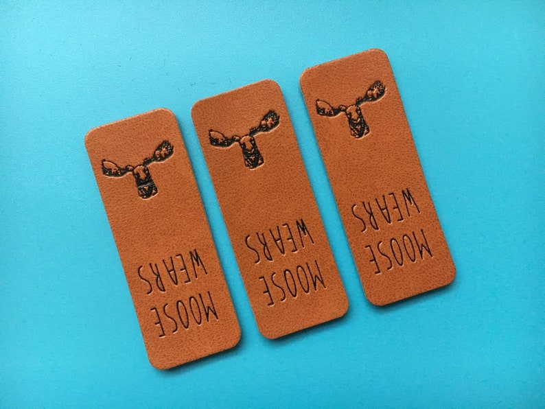 May include: Three brown leather labels with a moose graphic and the text "MOOSE WEARS" printed on each.