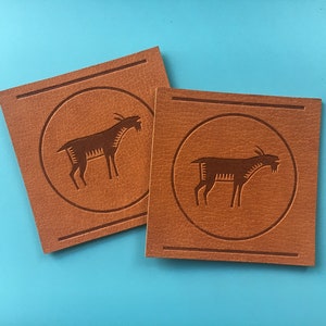May include: Two brown leather patches with a stylized goat design embossed in the center of each patch.