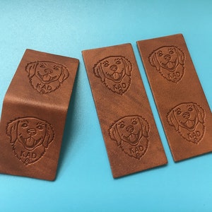 May include: Three brown leather labels with an embossed image of a golden retriever dog and the word "KAD" on each label.