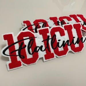Peut inclure: Une pile d'écussons en feutrine blanche présentant les lettres "ICU" en chenille rouge de style universitaire, avec le texte cursif noir brodé "flatlining" superposé. Les écussons ont une surface texturée et un contour blanc.