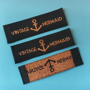 May include: Three black fabric labels with gold glitter lettering and an anchor symbol. The labels read "Vintage Mermaid".