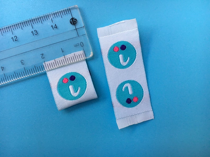 May include: Two white fabric labels with a turquoise circle containing the letter "I" and three small dots in pink, purple, and black.