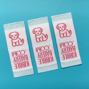 May include: Three white fabric labels with pink stitching. Each label features a pink silhouette of a dog and the text "KIBBLE BAKERY .COM".