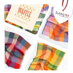 Può includere: Una collezione di campioni di tessuto con trama a nido d'ape caratterizzati da un motivo a quadri multicolore nelle tonalità arancione, verde, blu e rosso. Un cartoncino bianco riporta il testo WAFFLE A WIDE WIDTH COLLECTION e un'etichetta a cuore dice SuMa TEX.