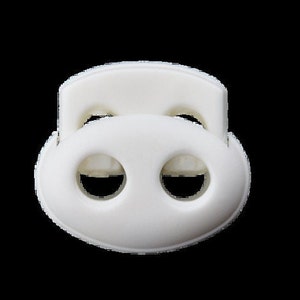 Puede incluir: Toggle de pl&aacute;stico blanco con dos agujeros. El toggle tiene forma ovalada y tiene un borde elevado en la parte superior.