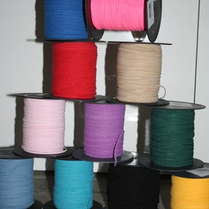 Op de afbeelding: Een verzameling spoelen met gekleurde elastiek, gewikkeld op zwarte plastic spoelen. De kleuren omvatten roze, blauw, rood, paars, groen, beige, zwart, geel en turquoise.