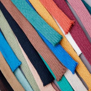 May include: Assortment of colorful cotton cords in various shades, including blue, green, yellow, orange, red, brown, and beige. The cords are arranged in a fan shape, showcasing their texture and color variations.
