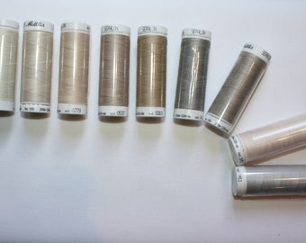 Può includere: Una collezione di dieci bobine di filo in diverse tonalità di beige e grigio. Le bobine sono etichettate "SEFALON" e hanno dei numeri.