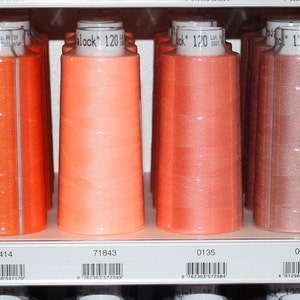 Könnte beinhalten: Ein Regal mit Garnrollen in verschiedenen Orangetönen, Rosa und Rot. Die Spulen sind mit Nummern und der Marke "Trelock" gekennzeichnet.