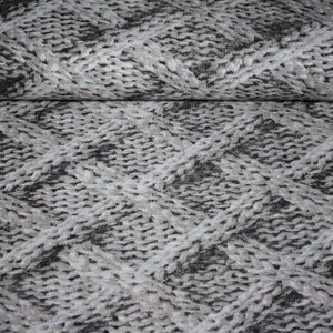 Könnte beinhalten: Nahaufnahme eines grauen und weißen Stoffes mit einem Zopfmuster. Der Stoff hat eine strukturierte Oberfläche und eine gewebte Optik.