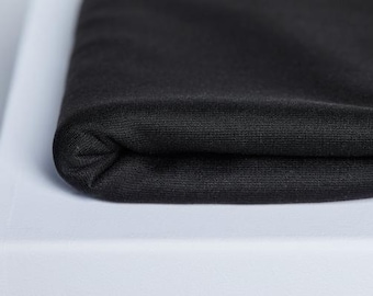 Peut inclure: Gros plan sur un tissu noir plié, probablement un textile. Le matériau présente un tissage fin et texturé et semble doux. Le bord plié crée une forme arrondie, reposant sur une surface blanche. Idéal pour la confection.
