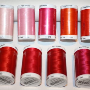 Könnte beinhalten: Zehn Garnrollen in verschiedenen Schattierungen von Rosa, Rot und Orange. Die Rollen sind mit "Poly Sheen" beschriftet und haben aufgedruckte Farbnummern.