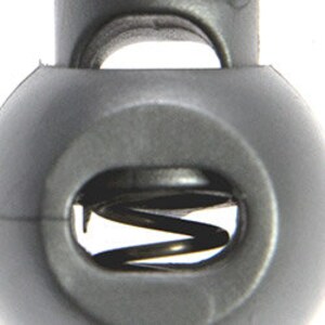 May include: Close-up of a black plastic toggle with a metal spring inside. The toggle has two holes for cord or string.