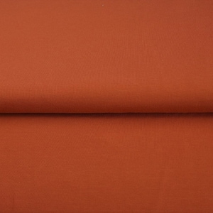Può includere: Un primo piano di un tessuto color ruggine. Il tessuto è liscio e ha una leggera lucentezza.