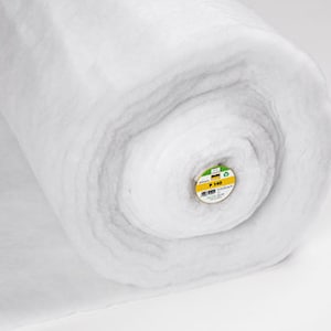 Puede incluir: Un rollo grande de guata blanca, enrollado firmemente. El material parece suave y esponjoso, con una superficie ligeramente texturizada. El extremo del rollo revela una etiqueta con texto y una combinación de colores verde y amarillo. El fondo es blanco liso.