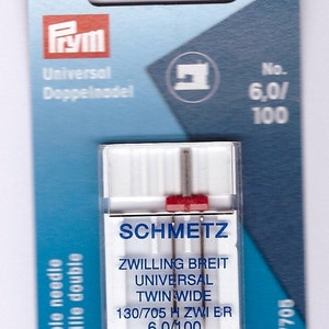 May include: A packet of SCHMETZ twin needles for sewing machines. The packaging is white and blue, with the brand name and needle specifications visible. The needles are labelled as 6.0/100, and the packet also includes the text "Double needle".